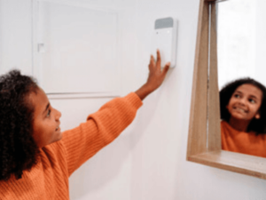 una bambina riflessa ad uno specchio cerca di accendere il termostato del riscaldamento sul muro